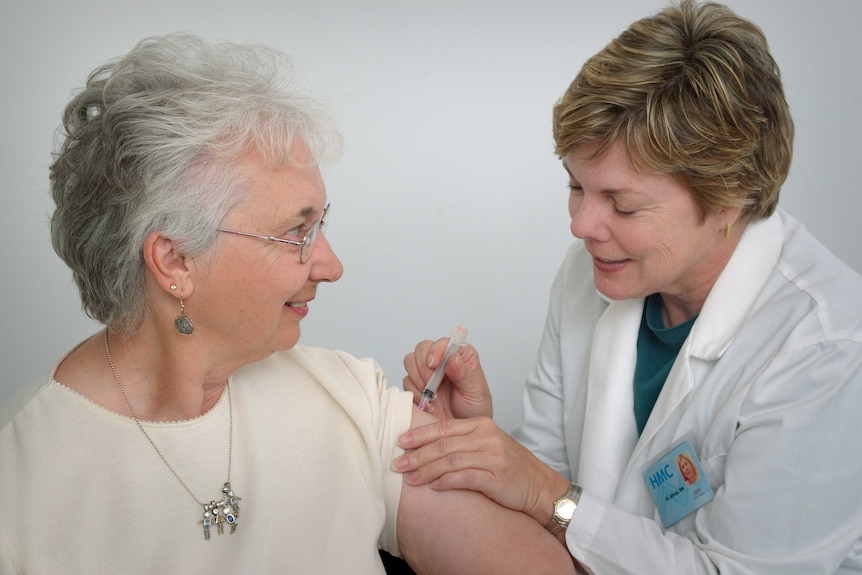A smiling woman gets a vaccine injected into her upper arm by a doctor