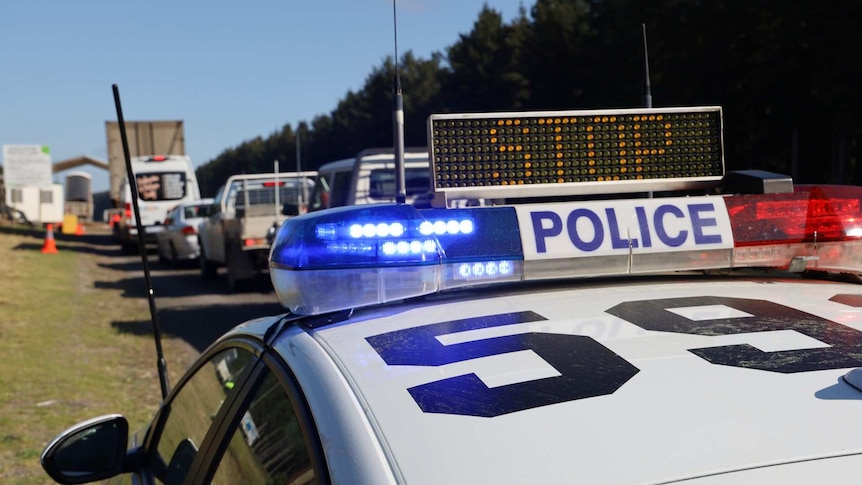 A "STOP" lights flash on a parked police car, as a line of cars and truck stretches into the distance