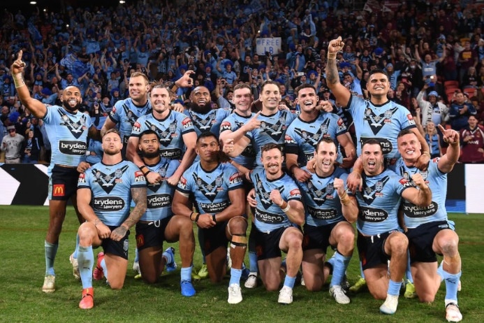 The New South Wales team in blue shirts celebrate thier series win with fans in the background.
