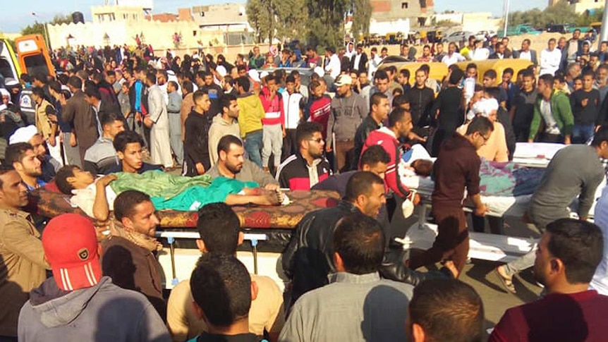 Injured people on stretchers are carried through a crowd.