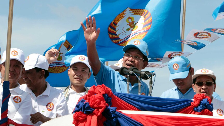 Cambodian Prime Minister Hun Sen waves to supporters as he speaks at a podium during an election campaign rally.
