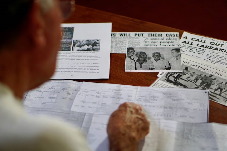 Over Bill Day's shoulder, newspaper clippings and genealogy shows Larrakia records.
