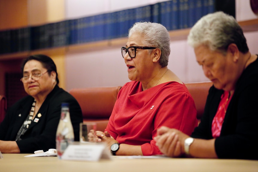 Three women sit a timber meeting table. 