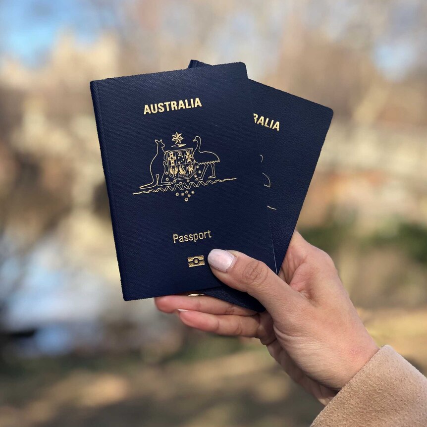 A hand holds two Australian passports.
