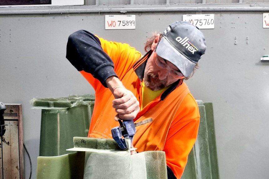 Man in high-vis and a cap runs a tool over a thick spout made of fibre glass
