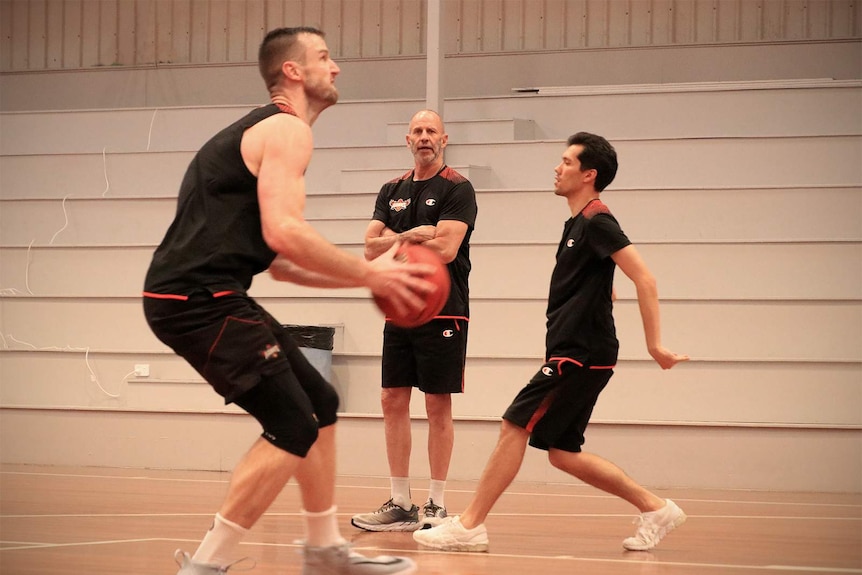Brian Goorjian watches on as AJ Ogilvy shapes to shoot a basketball at Hawks training.