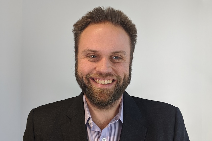 A profile image of a man with brown hair and a beard, wearing a shirt and dark suit jacket.