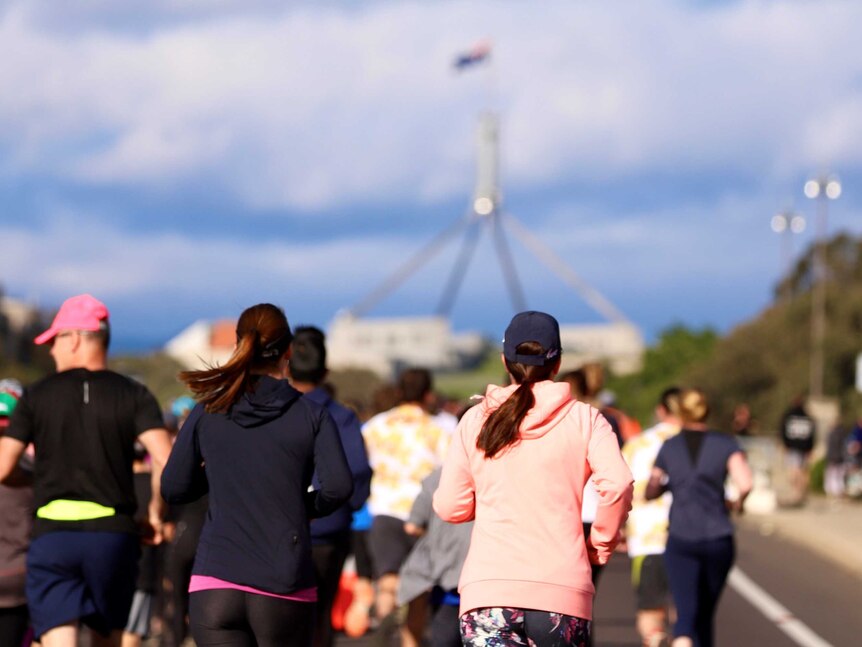 Joggers run on a main road leading up to Parliament House.