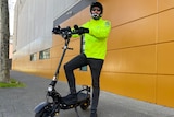 A man in high-vis and a helmet on an e-scooter on a city street.