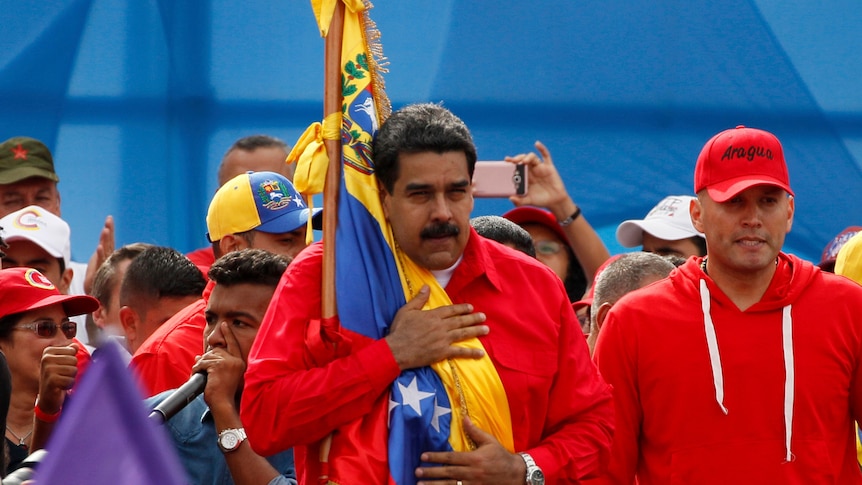 Venezuela's President Nicolas Maduro holds the Venezuelan flag, with his hand on his chest, during a rally in Caracas.