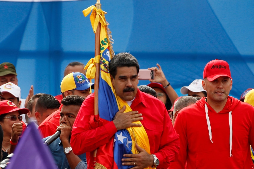 Venezuela's President Nicolas Maduro holds the Venezuelan flag, with his hand on his chest, during a rally in Caracas.
