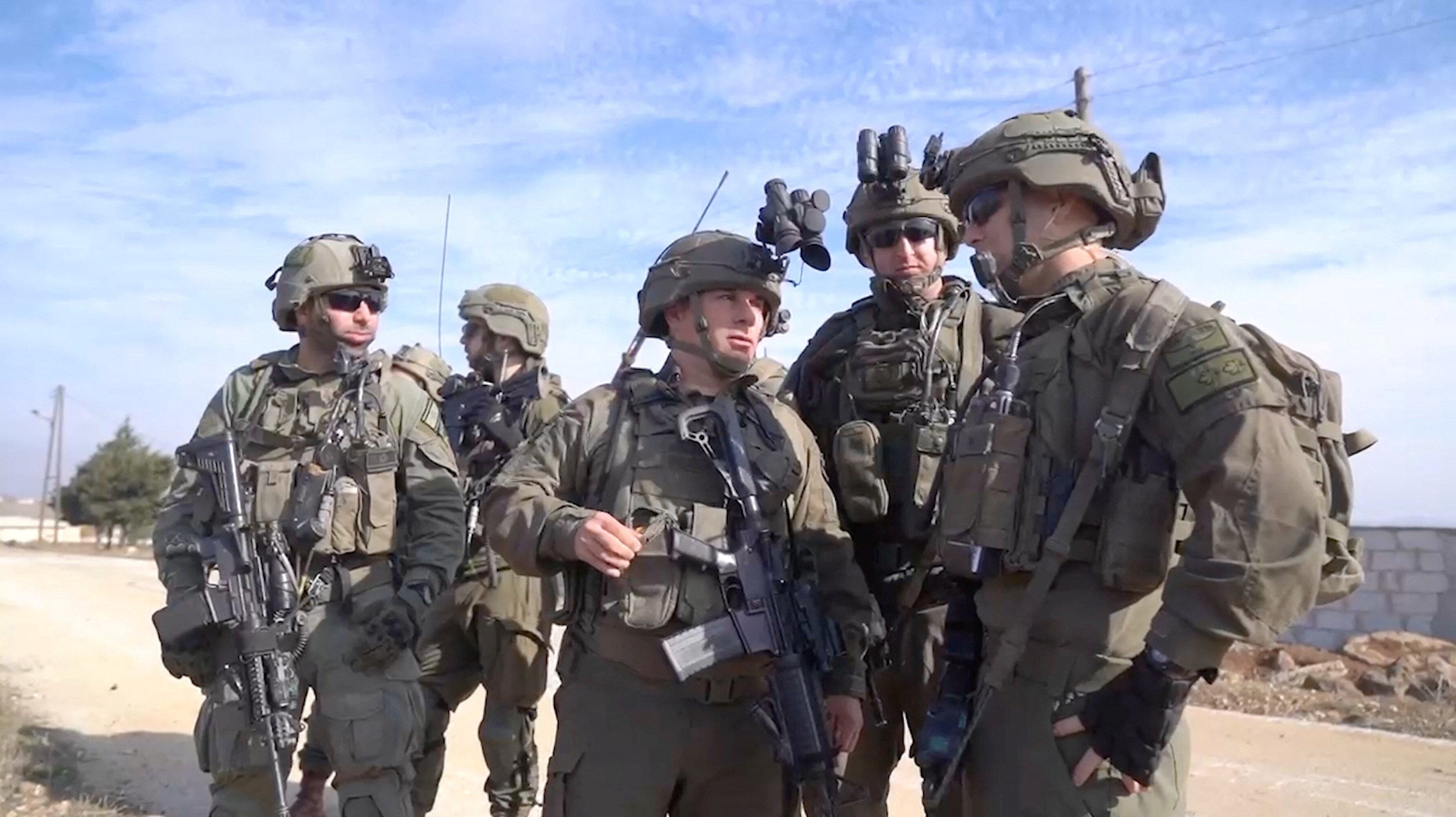 Five Israeli soldiers stand around looking at each other with four of them wearing sunglasses.