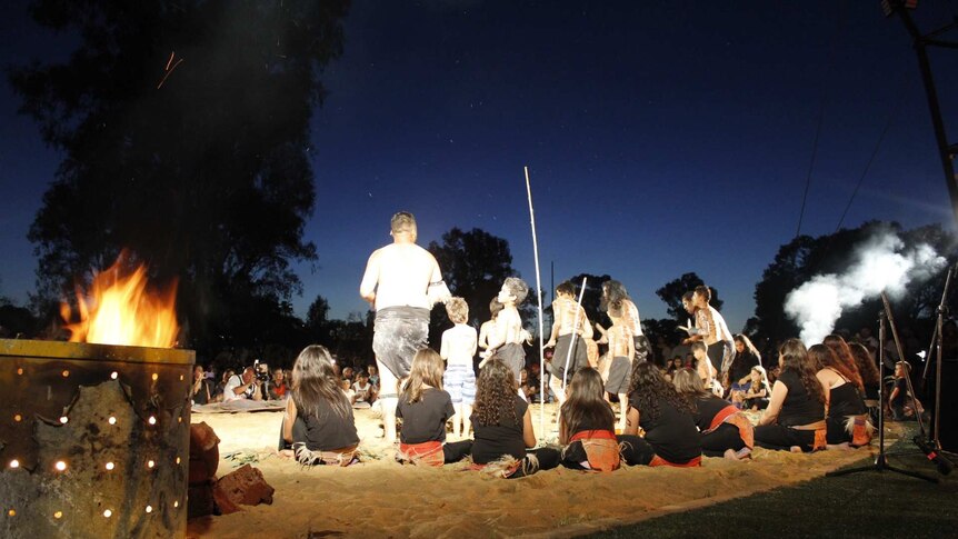 Indigenous dancers, mostly children, perform under a night sky.