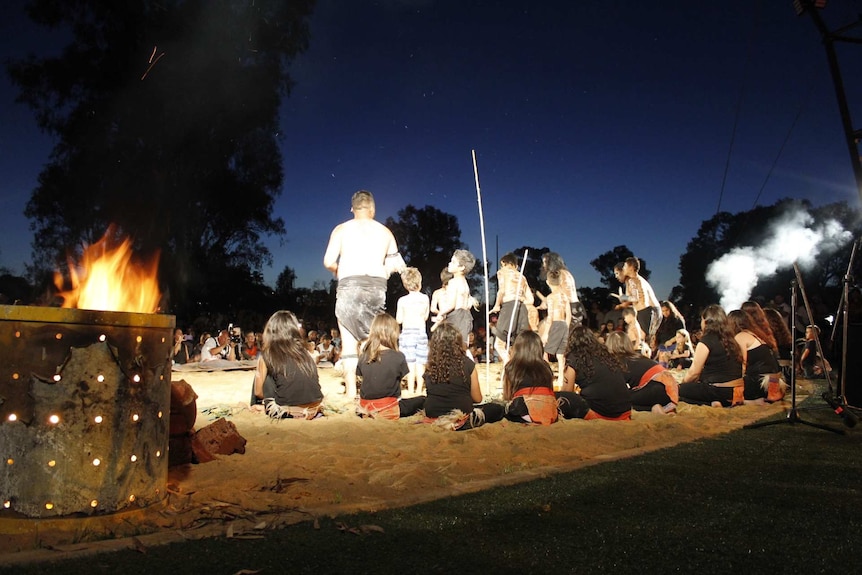 Indigenous dancers, mostly children, perform under a night sky.