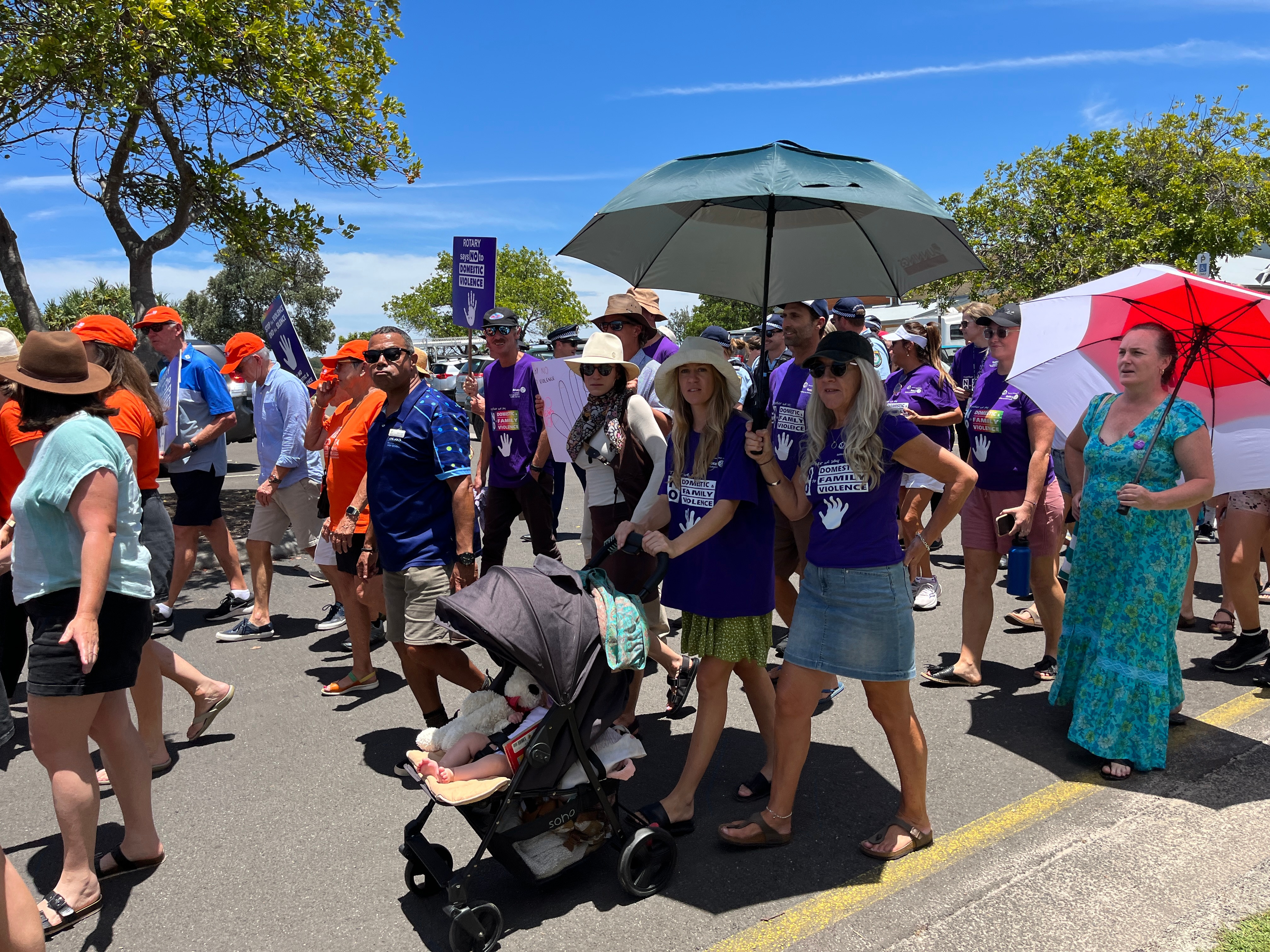 woman pushing a pram alongside her mother and a crowd of people marching