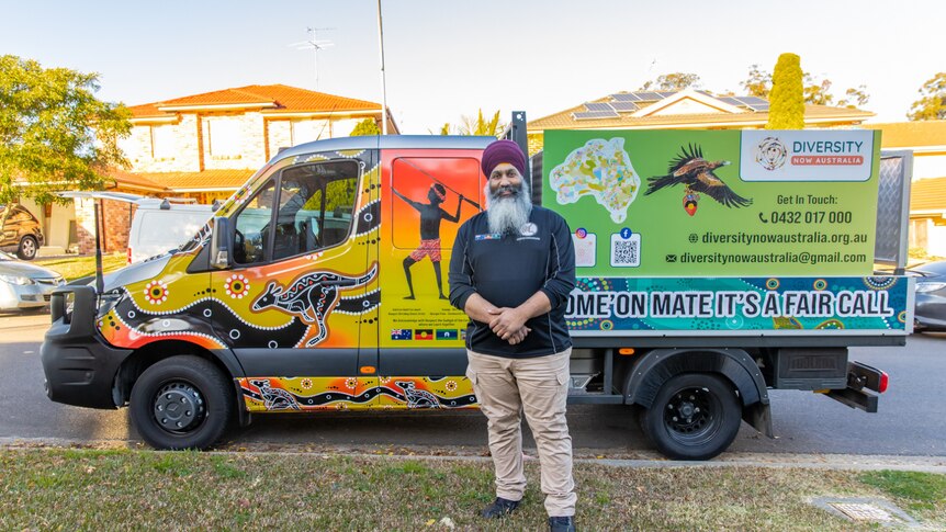 Amar Singh standing in front of a truck that is painted in Indigenous art 