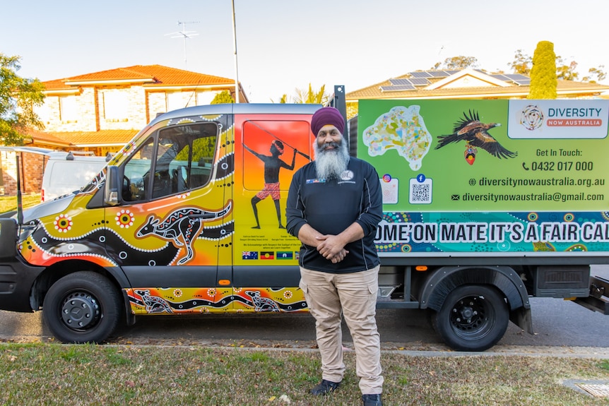 Amar Singh standing in front of a truck that is painted in Indigenous art 