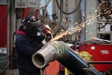 A worker, wearing a safety ask, engaged in pipe cutting work at a factory.