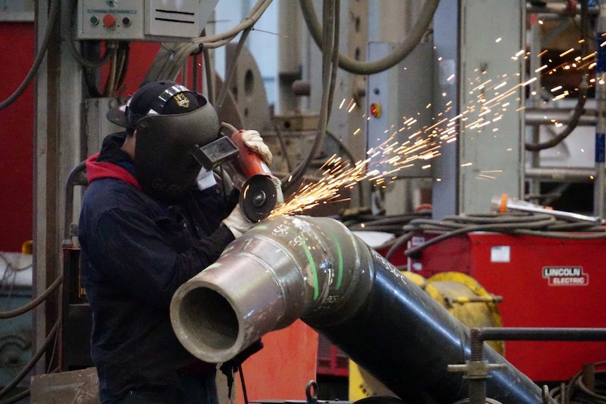 A worker, wearing a safety ask, engaged in pipe cutting work at a factory.