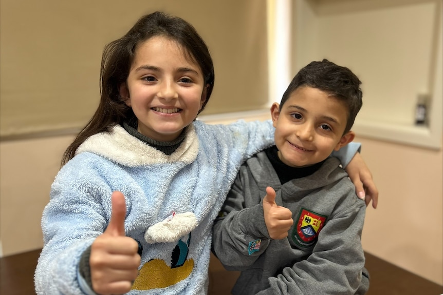 Young girl and boy with thumbs up, smiling at camera.
