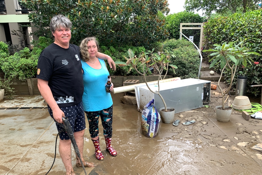 A man and woman hose their muddy patio.
