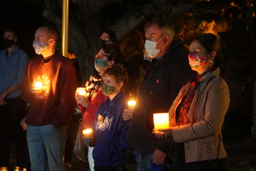 A group of people wearing masks and holding candles.