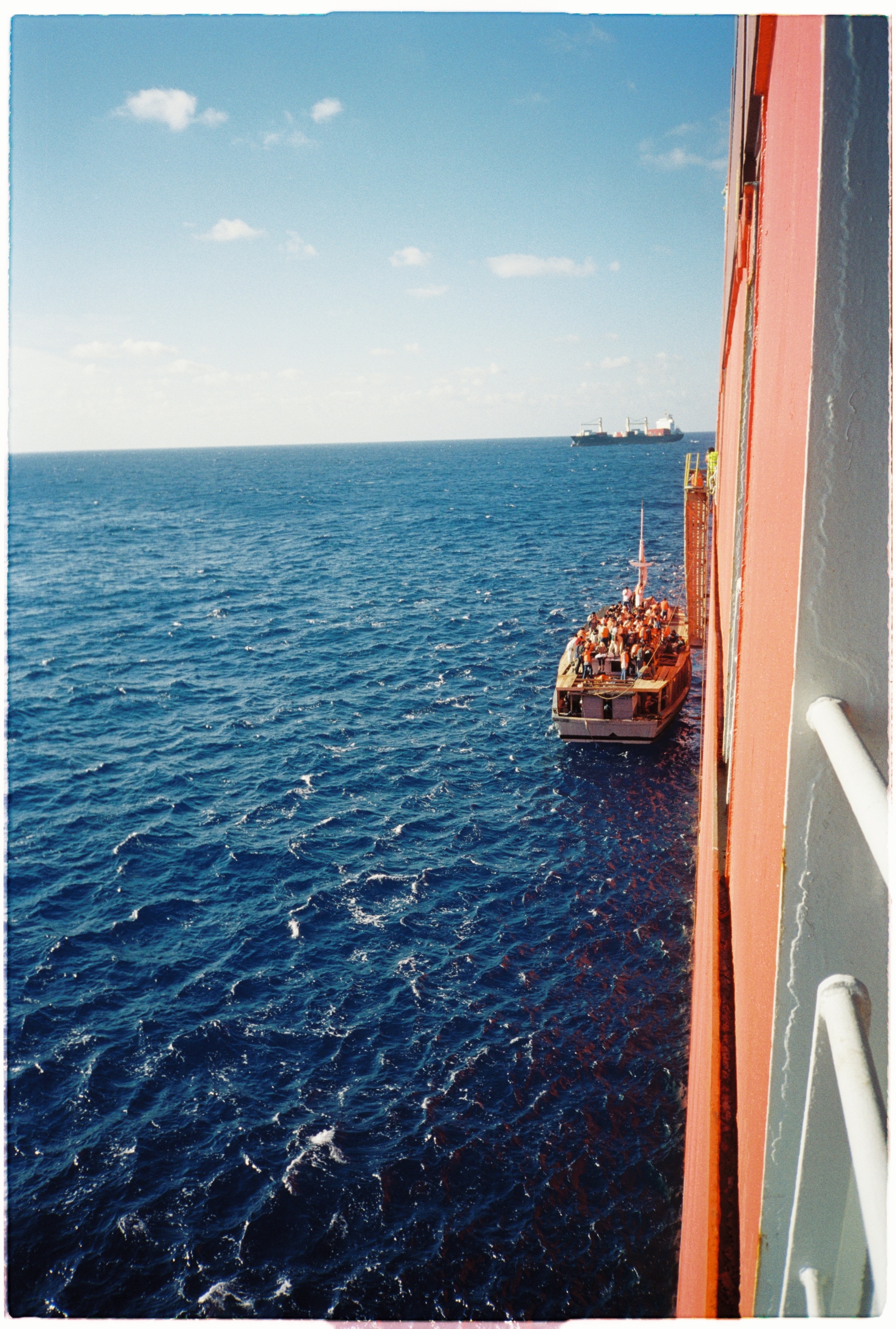 A small wooden boat pulls up to the side of a large freight ship.