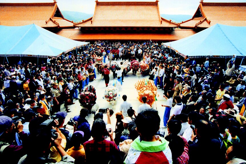 A large crowd gathers around a square in a buddhist temple with chinese dragons in the centre