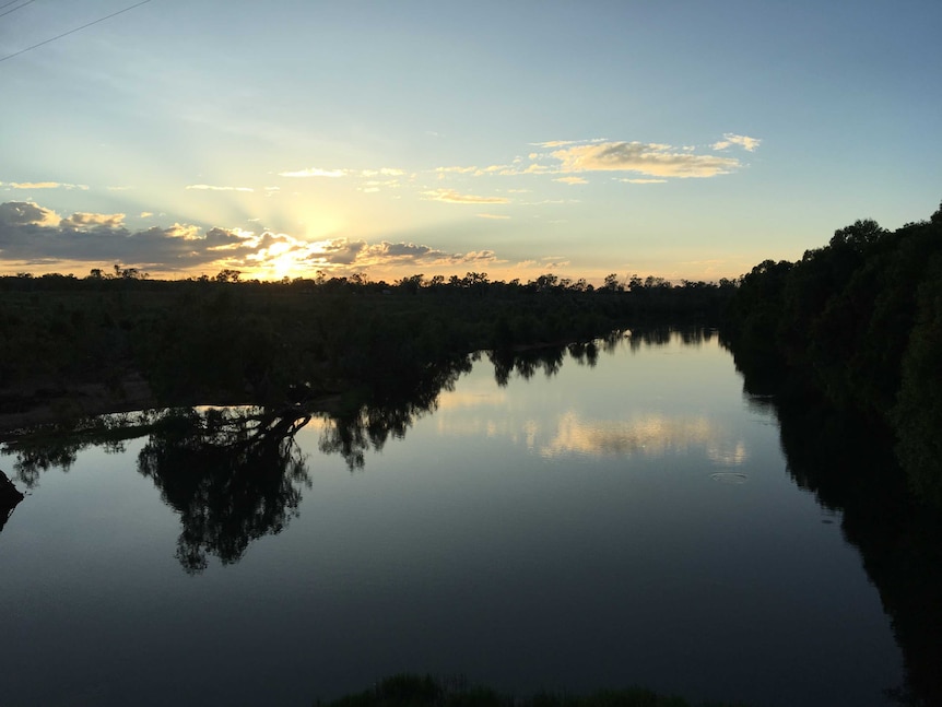 A river stretching to the horizon with the sun setting behind clouds on the left.