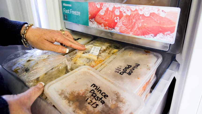 A stand up freezer with the door open showing draws full of containers filled with donated food.