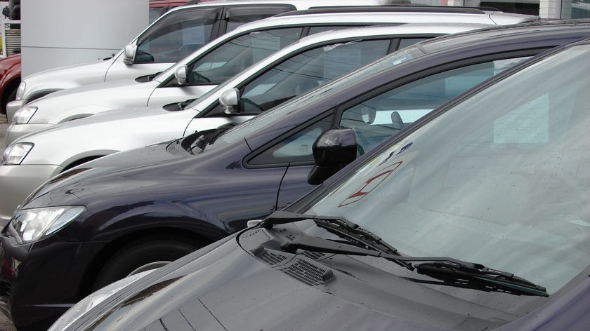 Three silver and two black cars parked in a line in a car yard.