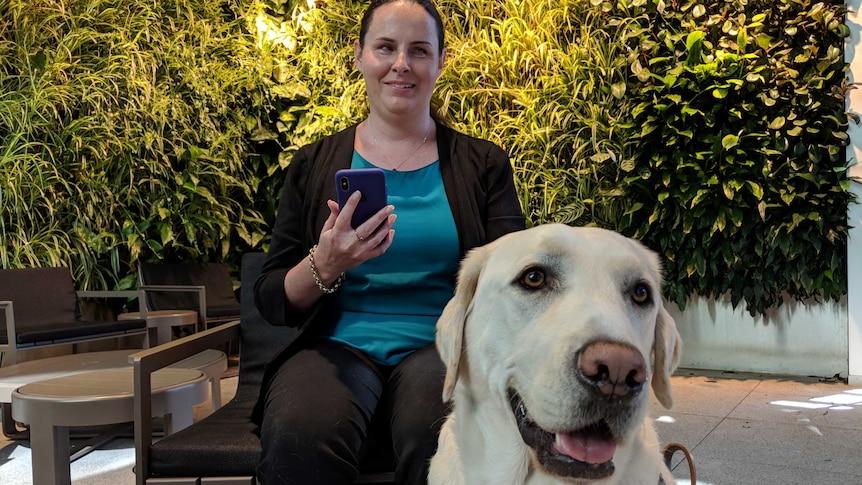 A vision-impaired woman holding a phone with a guide dog