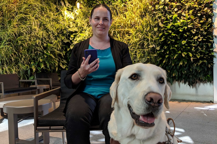 A vision-impaired woman holding a phone with a guide dog