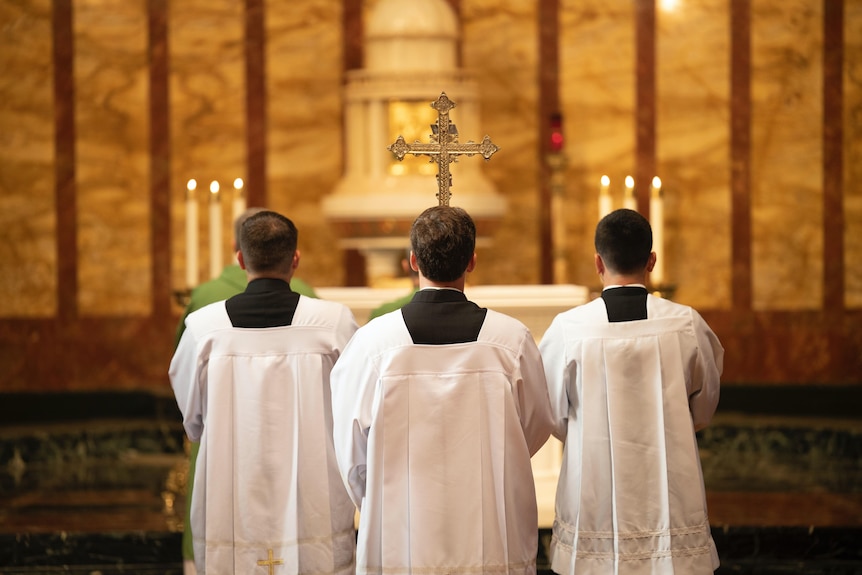 The backs of three priests praying in a church