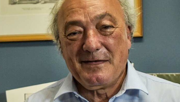 Middle aged man standing in office with grey hair and half smile.