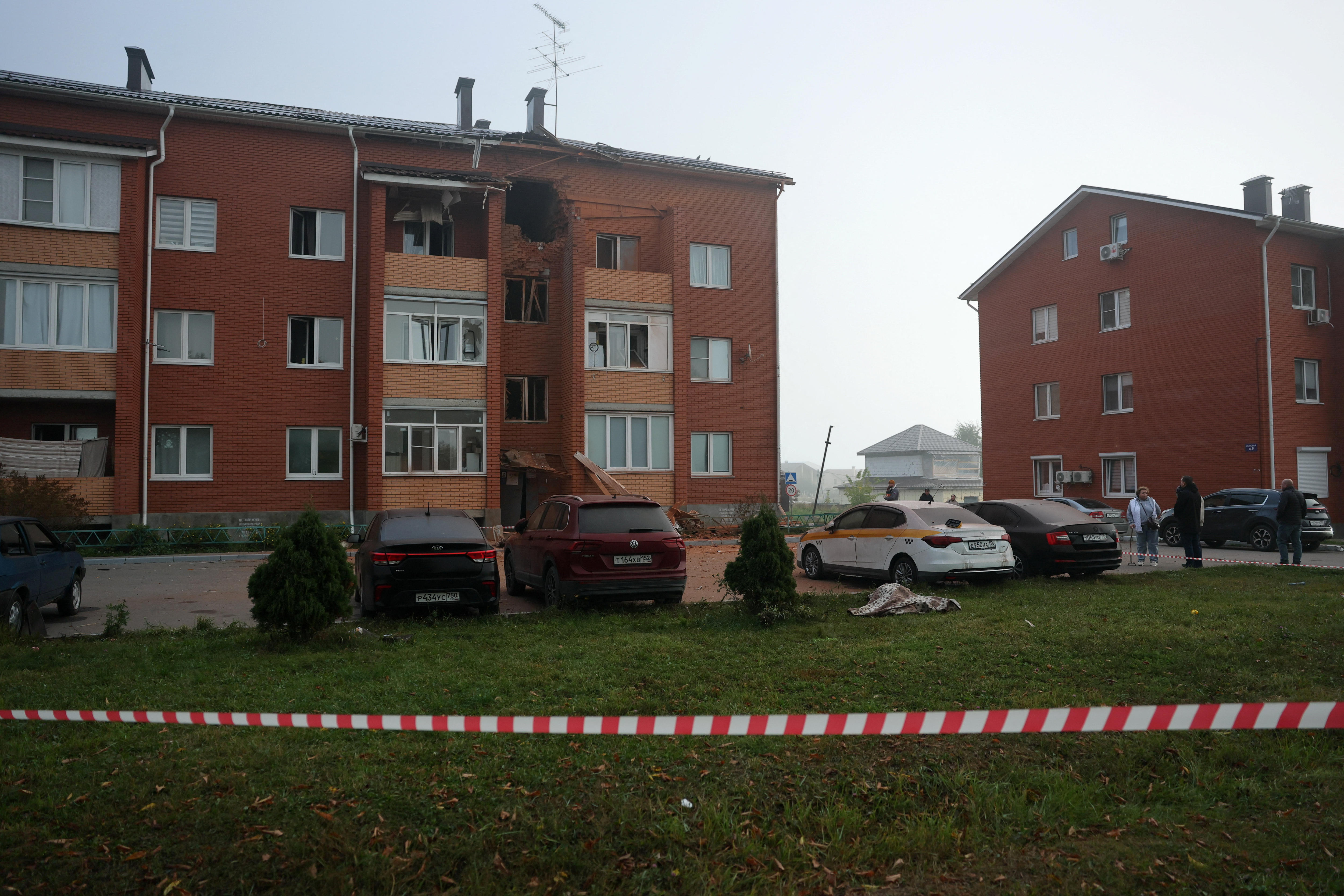 A three-storey apartment building has a hole in its outside wall from a drone strike, police tape can be seen out the front.