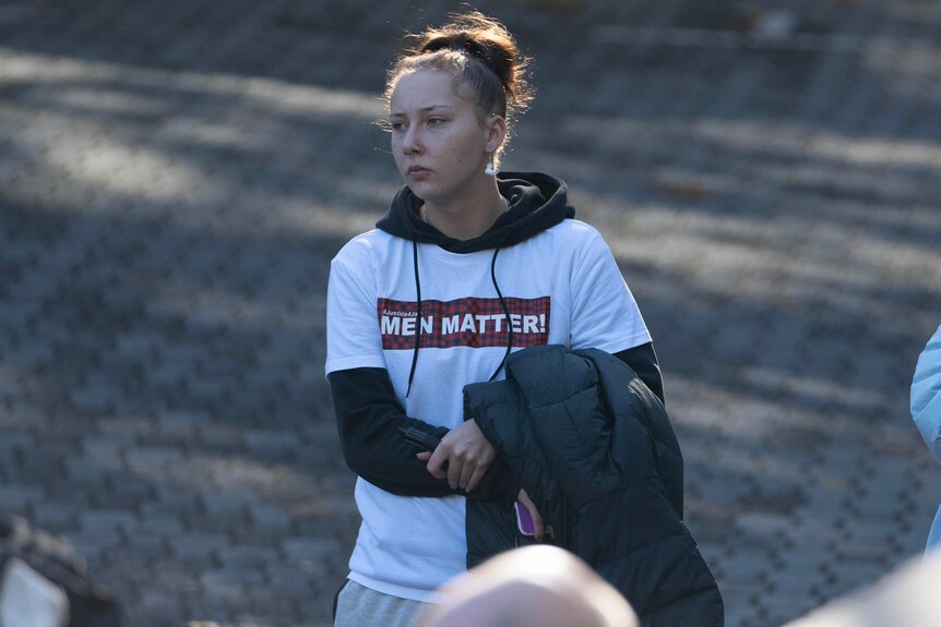 A woman wearing a shirt that says 'Men Matter' folds her arms outside a court building.