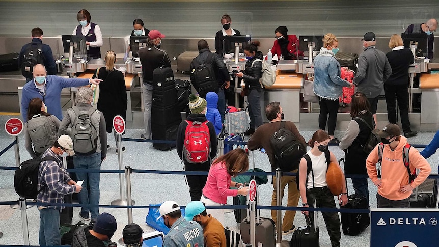 A group of people with their luggage bags stand in line at an airport wearing masks.