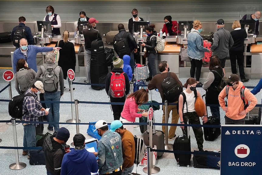 A group of people with their luggage bags stand in line at an airport wearing masks.