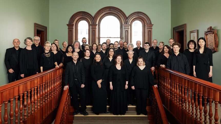 choir dressed in black posing on stairs in front of three arched windows