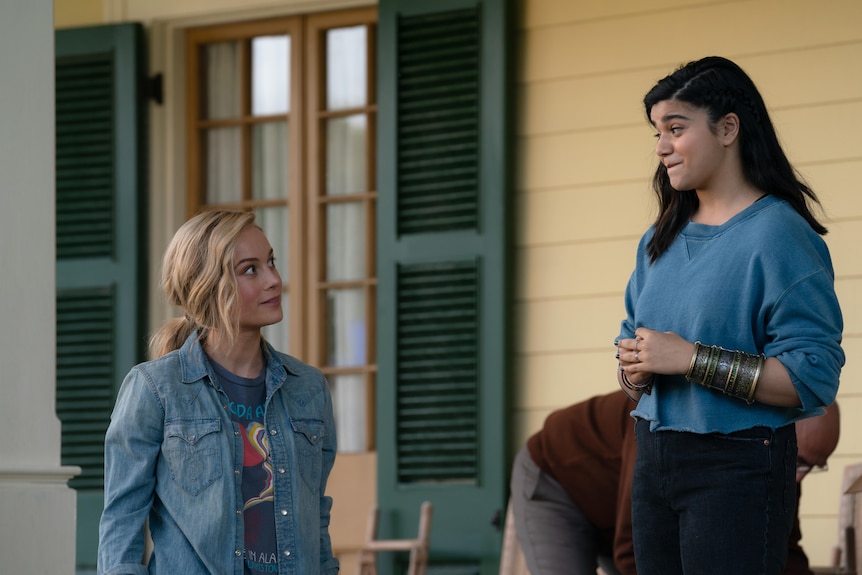 A blonde white woman in a denim jacket looks expectantly at a young Pakistani American woman with dark hair in a blue jumper.