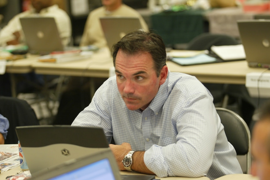 Billy Beane sits at a desk in front of a laptop.