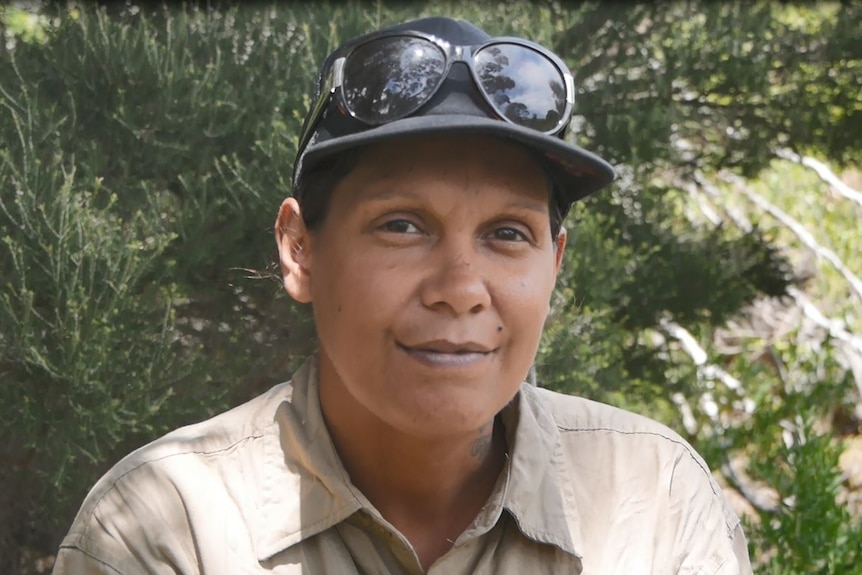 She sits in the bush wearing a cap