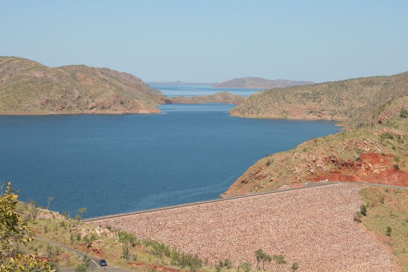 A huge dam wall and water in red rocky Kimberley country.