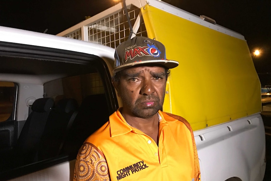 Simon Johnston wear a yellow night patrol jacket, and stands next to a van at night.