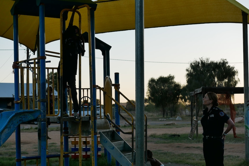 Kids play on a playground in a town camp with a police office looking at them, happily