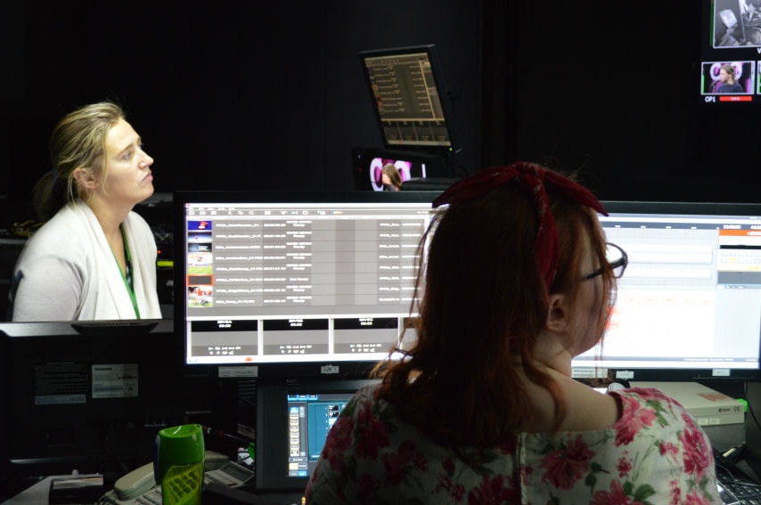 Butselaar left of screen and director in foreground in control room looking at monitors and computer screens.