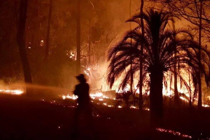 The silhouette of a fire fighter watering down a blaze.