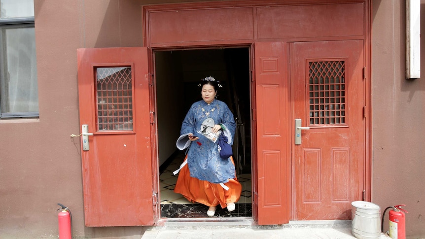 A woman leaves a red building in traditional Han Chinese clothing.