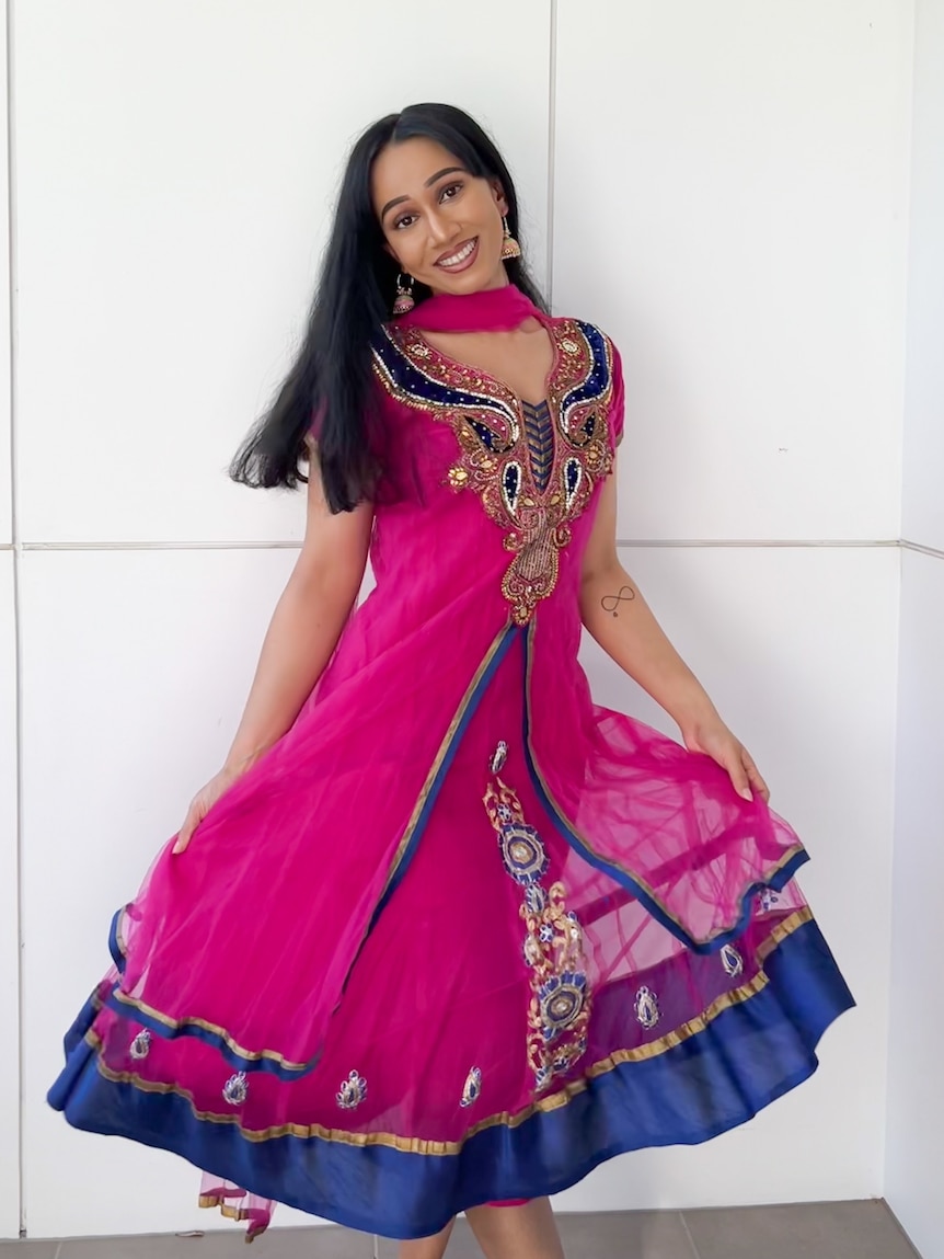 A woman poses wearing a pink anarkali, a garment like a knee-length dress.